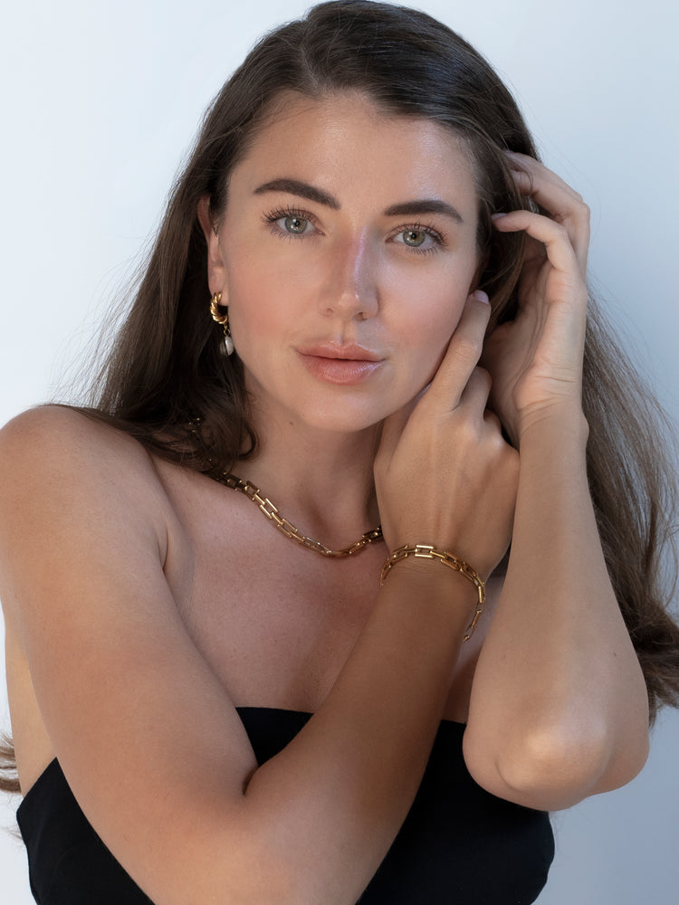 Model wearing a gold chain necklace, matching bracelet, and pearl drop earrings
