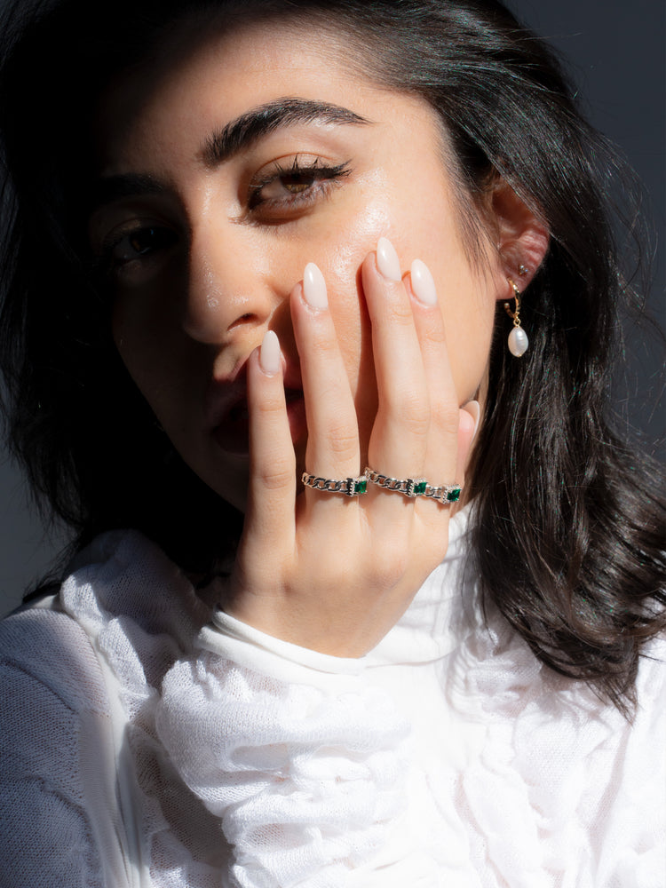 Woman wearing miramira emerald gemstone rings and a freshwater pearl gold earring